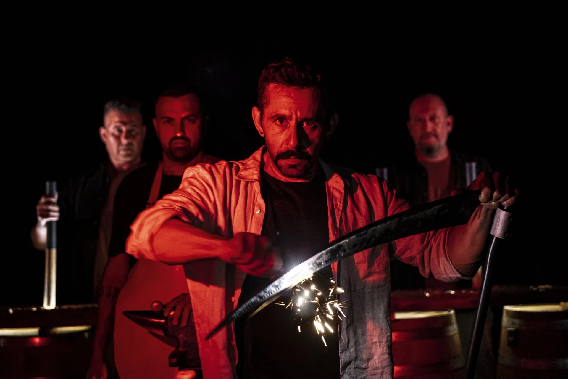 Actors forging with a scythe under red light